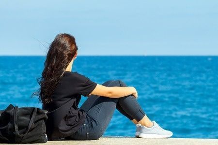 45866342 - young girl sitting on the edge of the pier and watching the blue sea.
